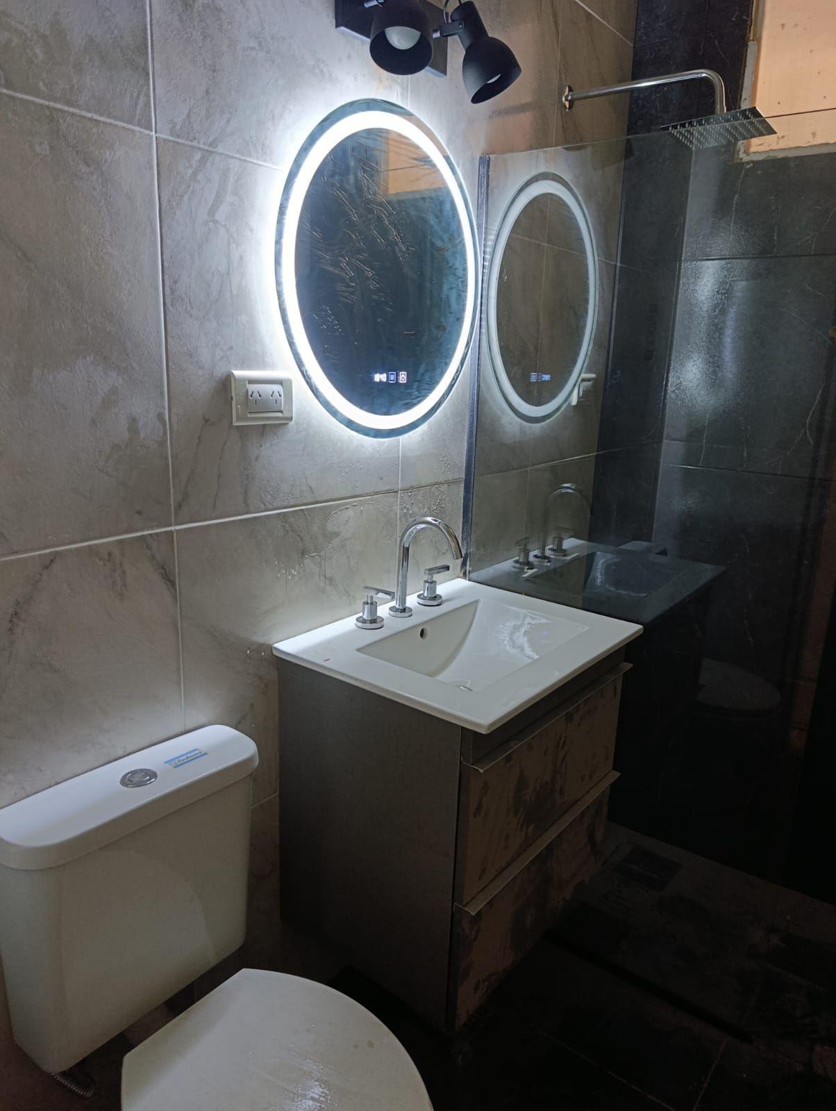 Baño terminado con vanitory, espejos con luz y revestimiento gris